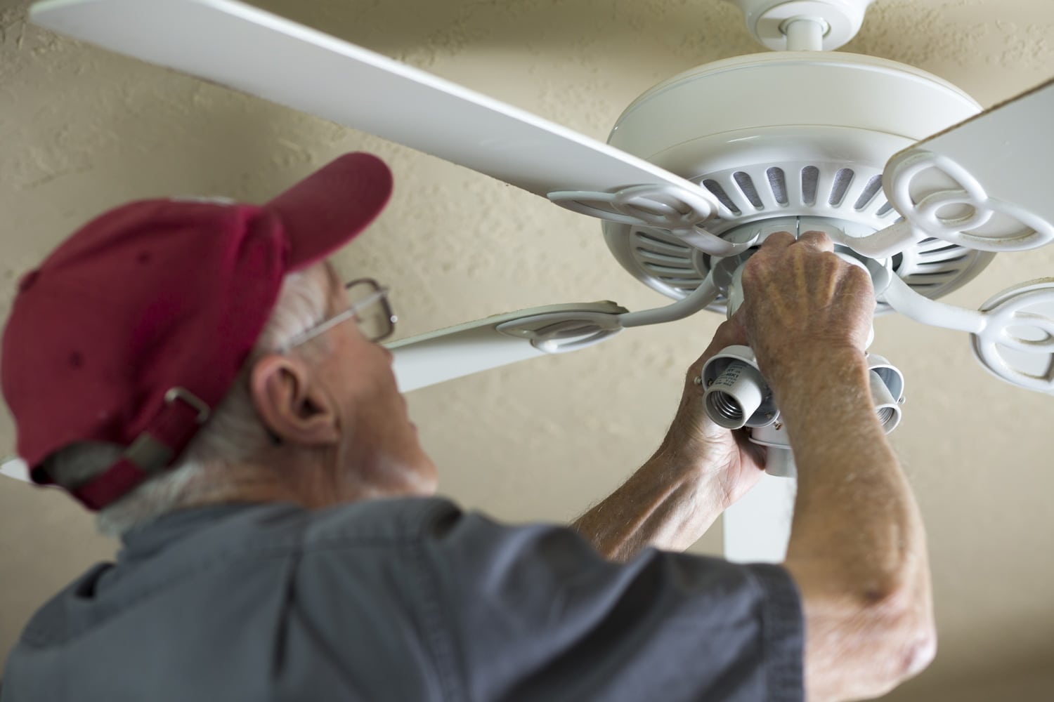 Electrician repairing ceiling fan for neighbor. He replaced the motor for the fan. Blue collar Caucasian senior man is retired but is still active and enjoying doing small repairs for others.