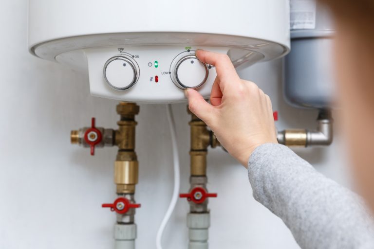 Female hand puts thermostat of electric water heater (boiler) in economy mode. Household enegry saving equipment - How Long Does A Water Heater Last