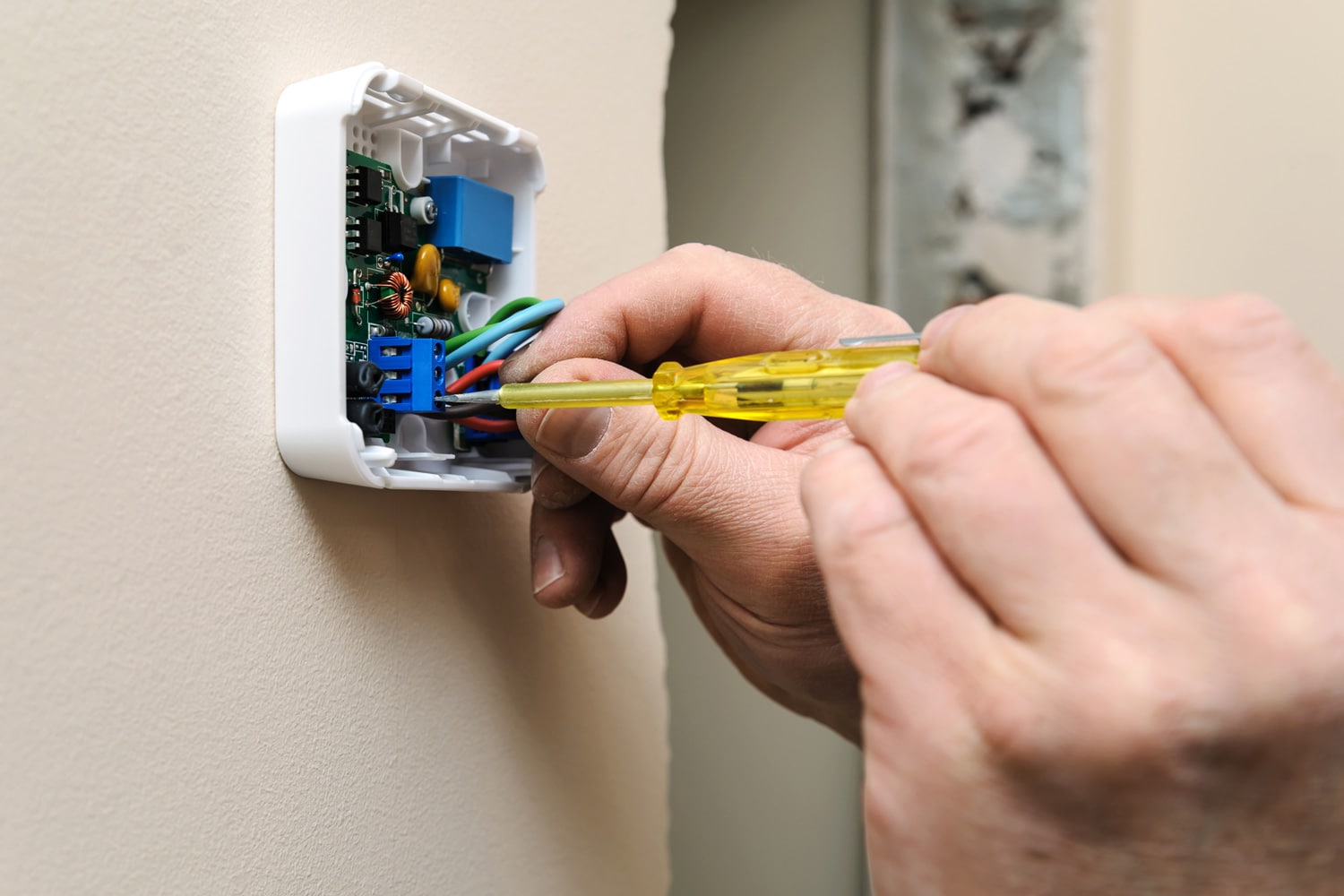 Installing a programmable room thermostat. Man's hands fixing the wires to the terminals and connects the device.