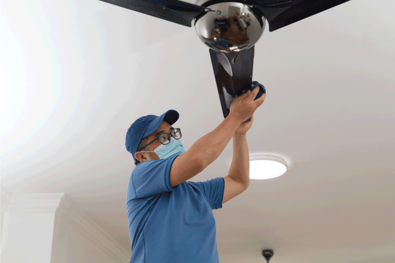 Low-angle-view-of-an-man-cleaning-ceiling-fan-at-home.-Can-A-Ceiling-Fan-Hold-A-Person