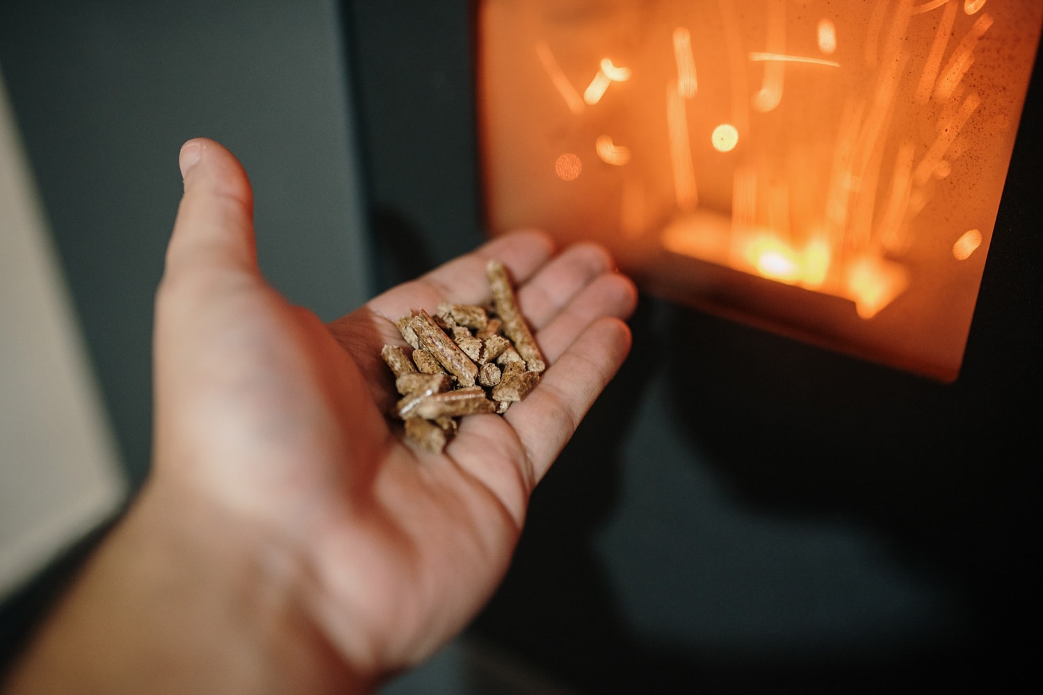 Pellet Biomass heating - Human hand holding biomass pellets by a fireplace