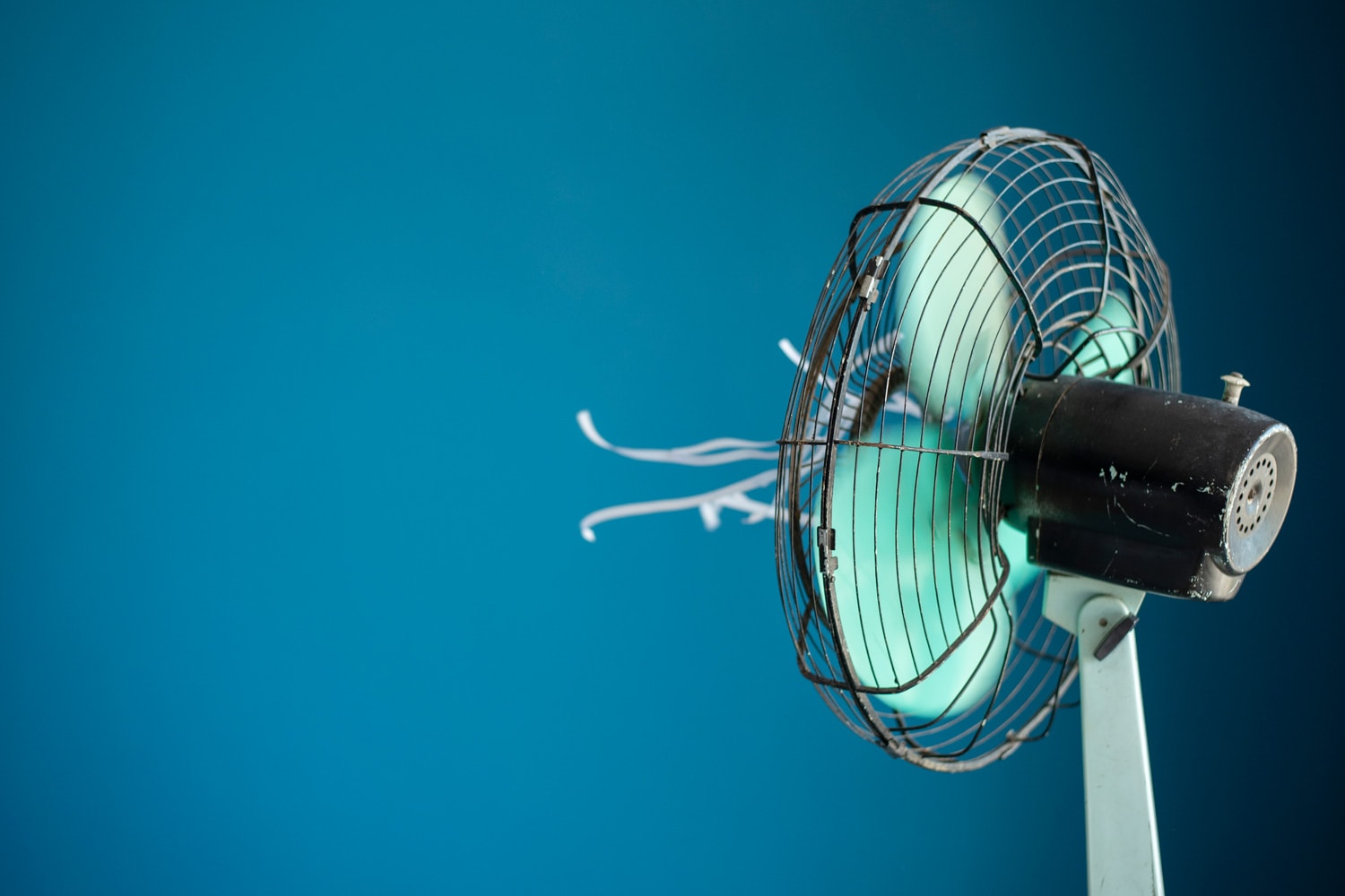 Shot of a metal electric fan with white streamers attached against a blue background