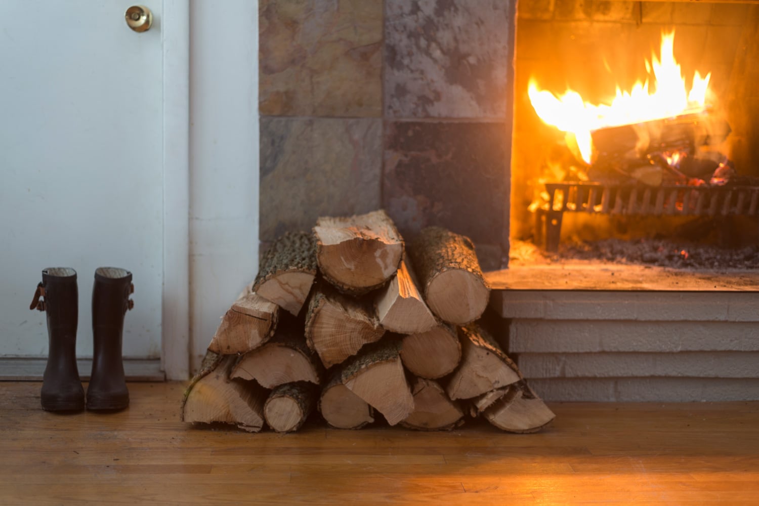 Slate titled fireplace with wood stack and boots by the door.
