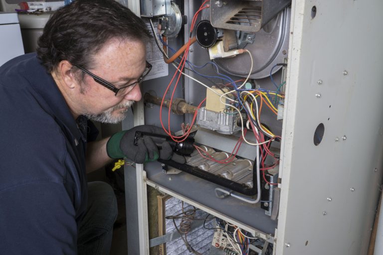 Technician looking over a gas furnace with a flashlight before cleaning it, Furnace Blower Not Working—What's Wrong?
