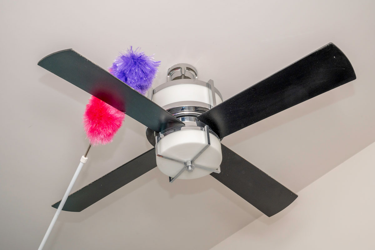 duster being used for cleaning the ceiling fan above the wall