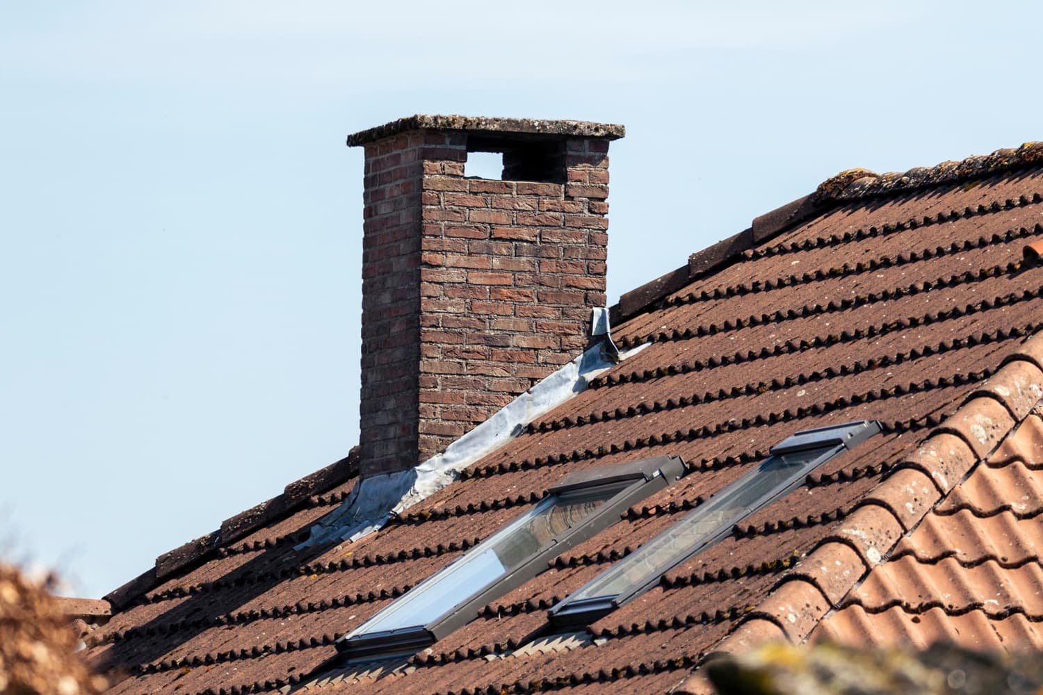 A portrait of a chimney on a roof of a house. The roof has ceramic tiles 