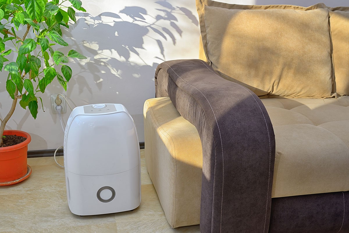 A small white portable air conditioner on the side of a couch