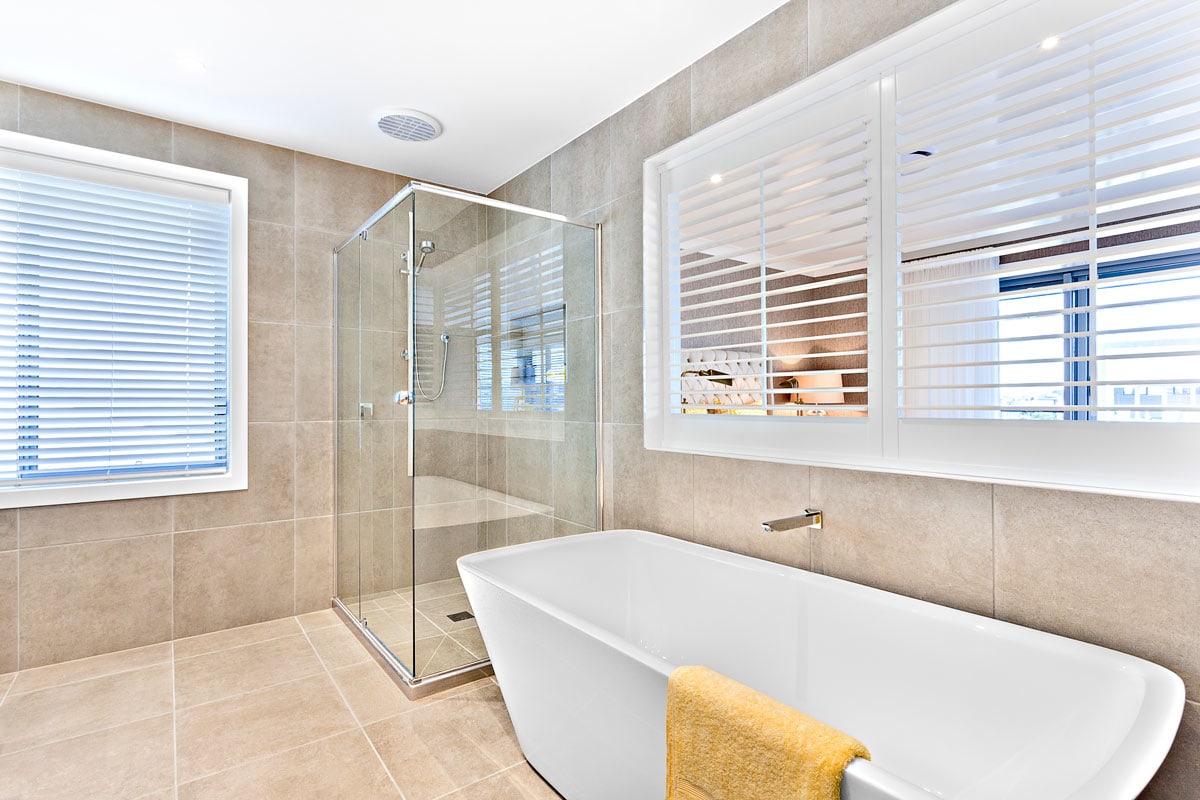Bright and modern designed bathroom with brown tiled flooring, glass shower wall and and white bathtub