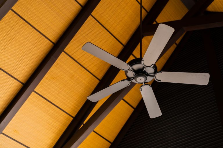 Brown indoor ceiling fan on an exposed wooden support beam, with a decorate wooden ceiling, in the hall of living room of a contemporary home interior, Why Is My Ceiling Fan Running So Fast?