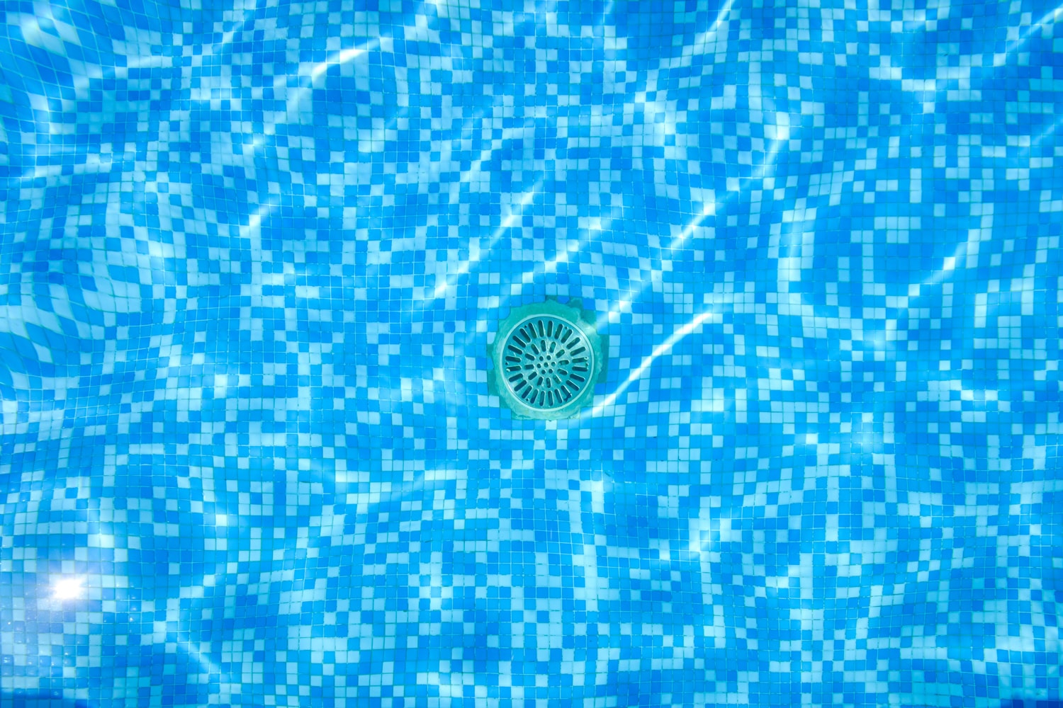 Drain of a pool, seen through the water from above.