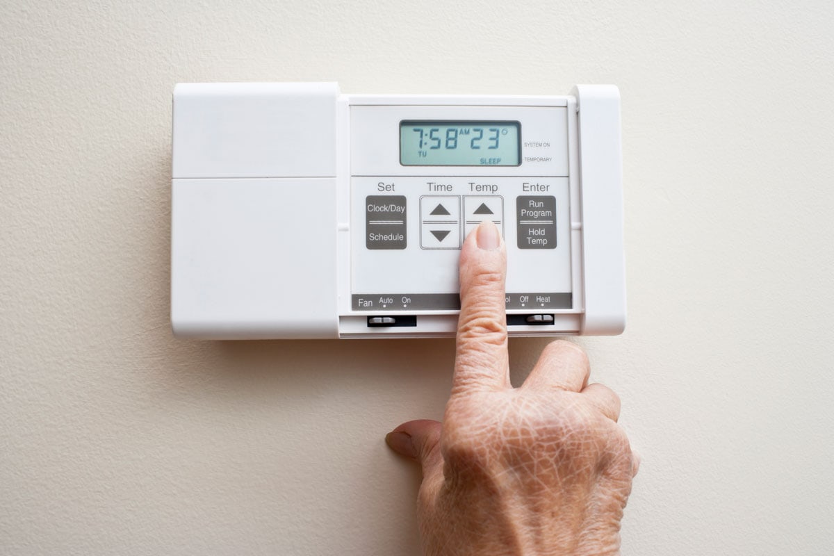 Elderly senior presses the button to turn down the thermostat