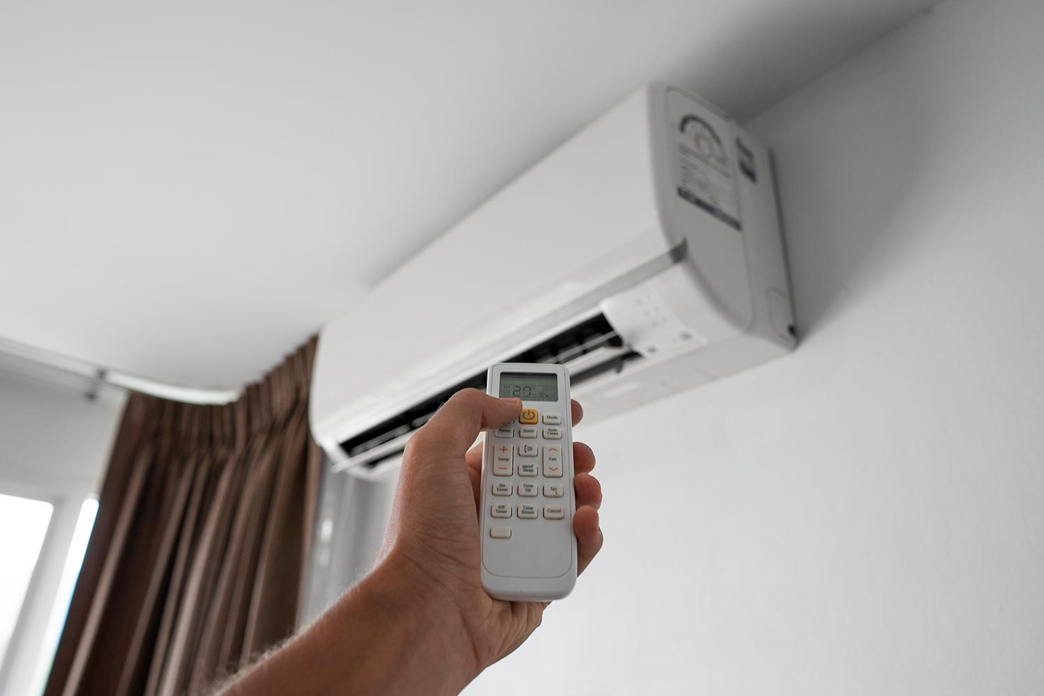 Hand holding rc and adjusting temperature of air conditioner mounted on a white wall