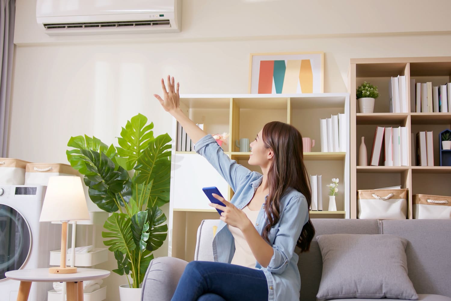 IOT smart home system concept - young woman using app on mobile phone to turn on air conditioner in living room