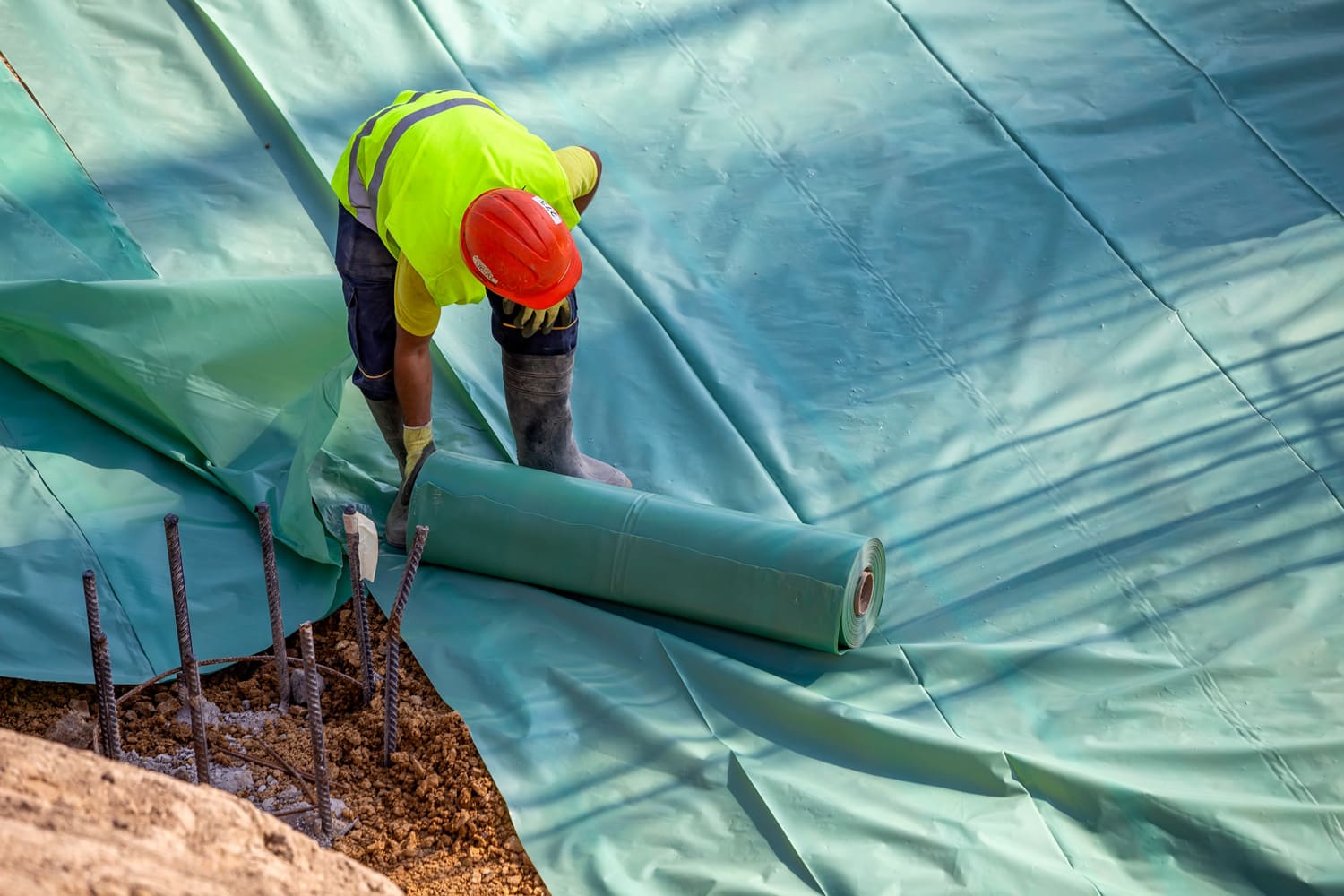Installing plastic vapor barrier before pouring concrete slab, helping to prevent moisture from migrating up from the dirt and creating a wet slab.