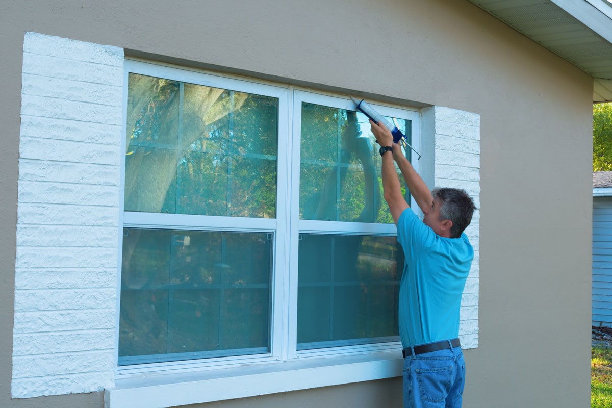 Man applying caulk to the weatherproofed windows
