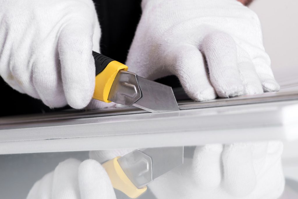 Master hands in gloves cutting white Foamex PVC foam board with utility knife.
