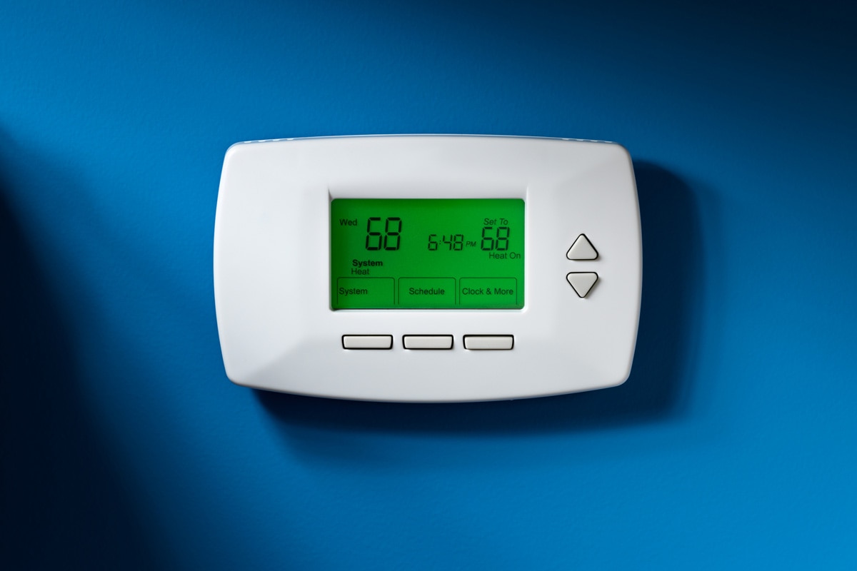 Programmable thermostat set to 68 degrees. Isolated on blue background with dramatic lighting.