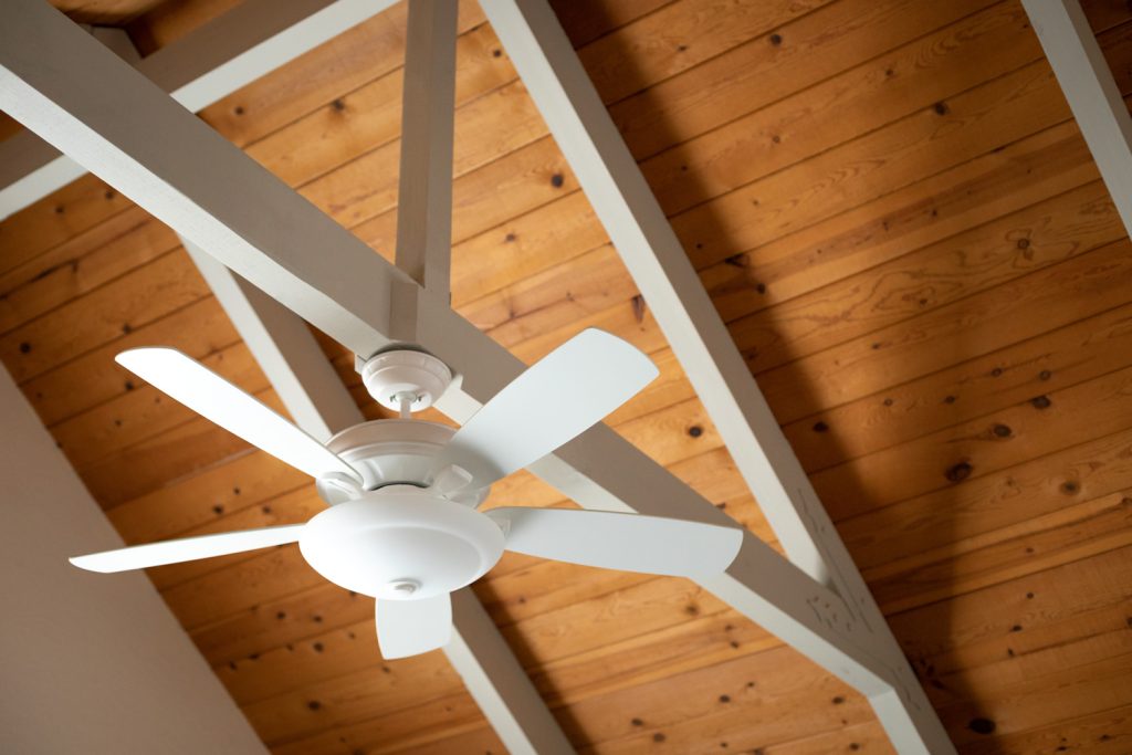 White ceiling fan on an exposed support beam, with a vaulted wood ceiling, in the living room of a modern home, with space for text on top and right side