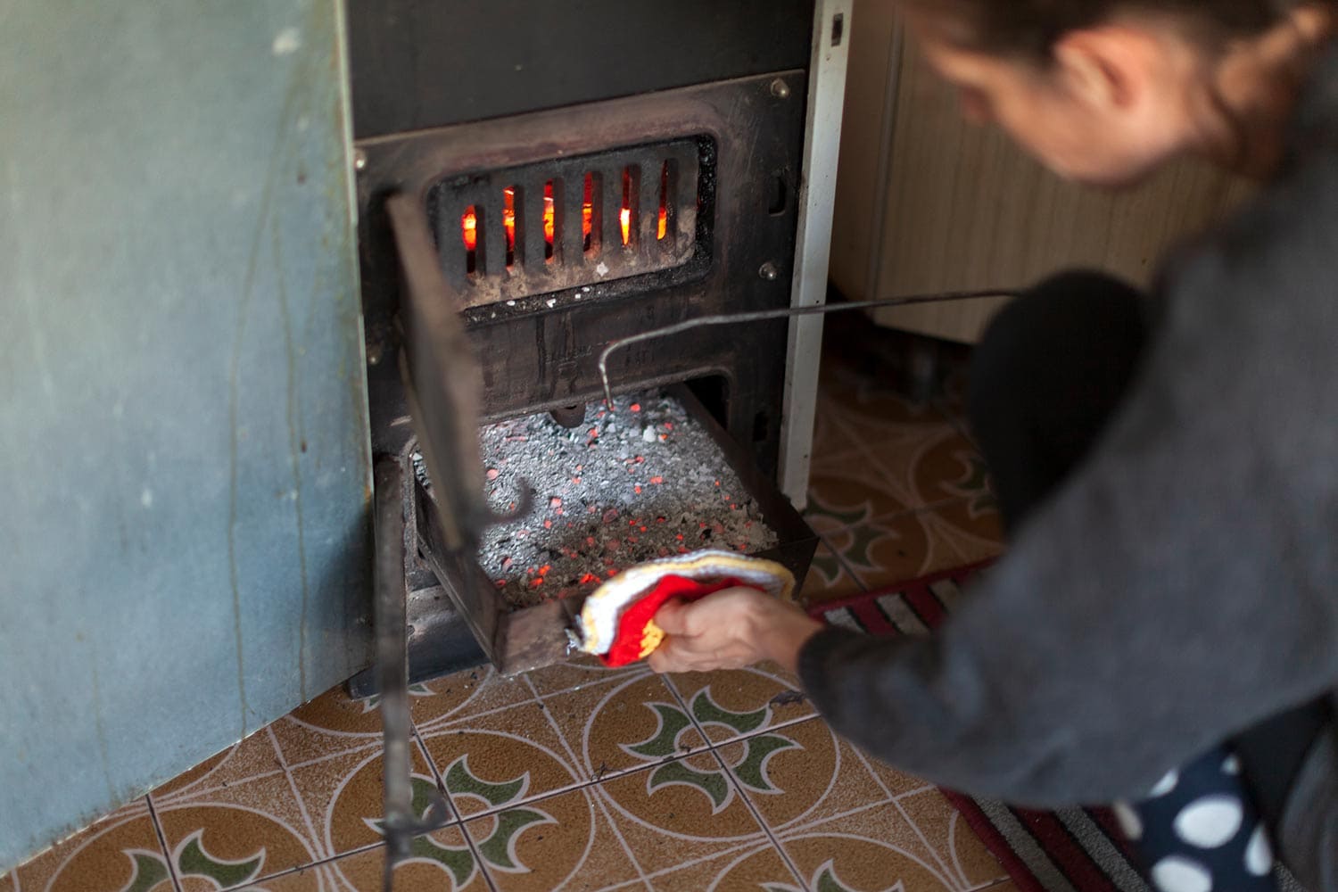 Woman taking full ash container out of wood burning stove in kitchen