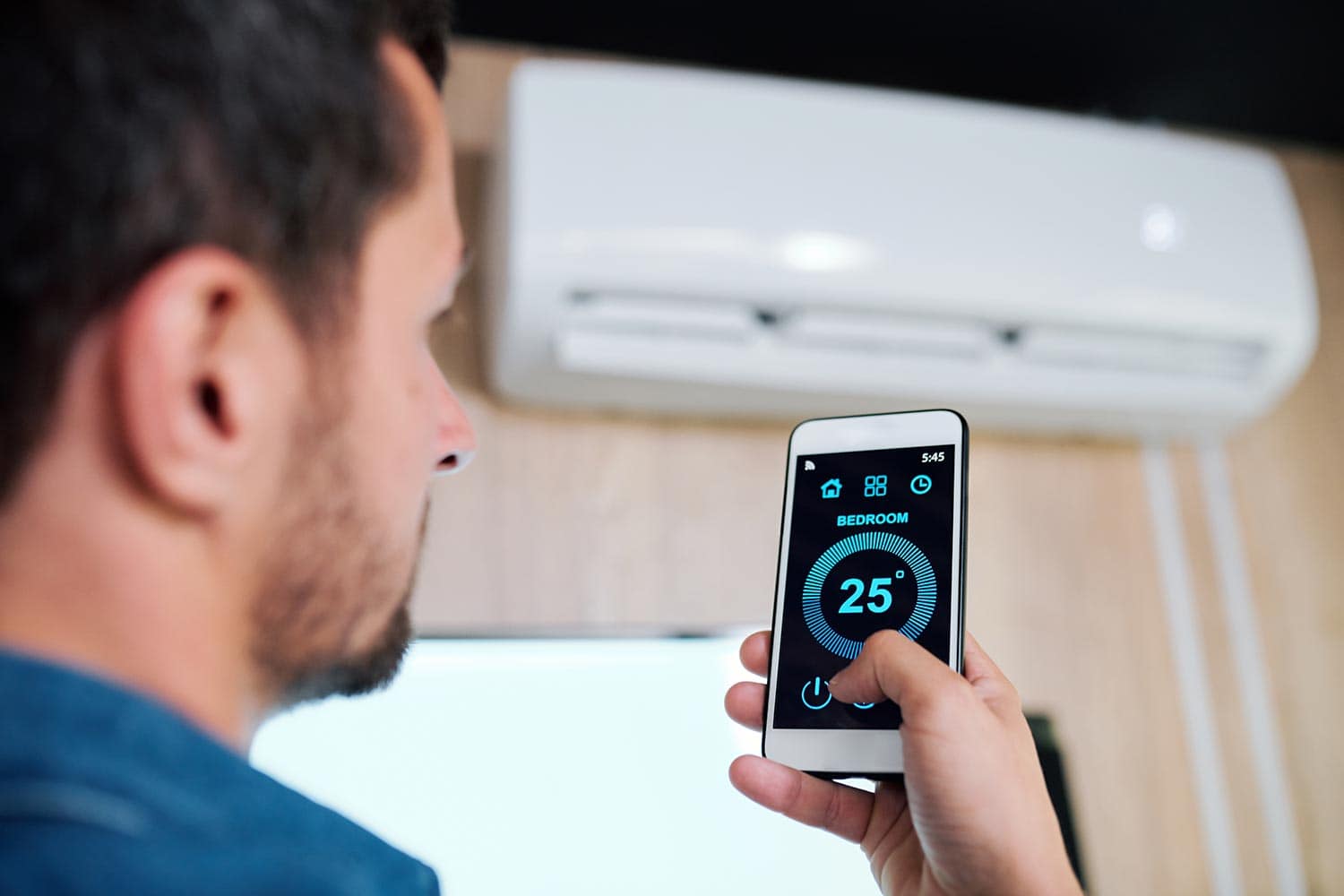 Young man using smart application to adjust temperature of air conditioner