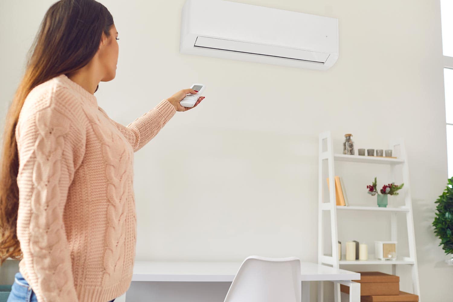 Young woman standing in living-room and switching on air conditioner