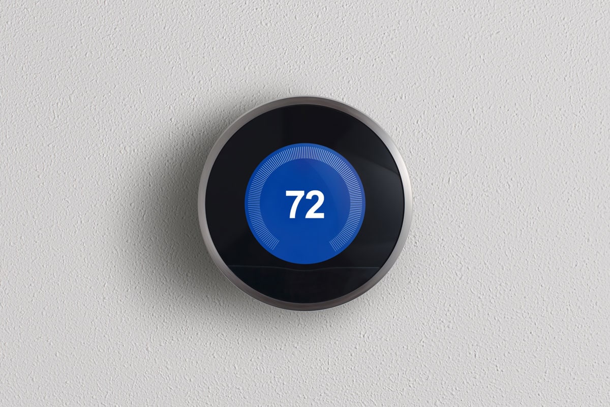 a round, modern, programmable digital thermostat, on a clean white wall in cooling mode