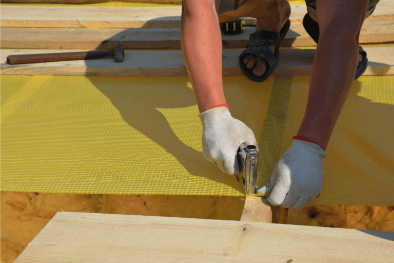 building contractor in protective gloves is installing waterproofing vapor barrier using a staple gun while roofing construction. Does A Warm Roof Need Ventilation