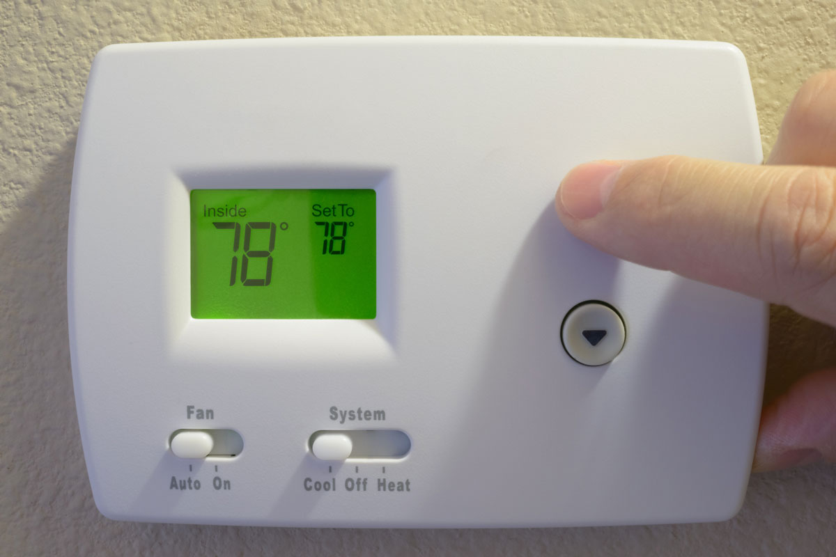 man's hand adjusting home thermostat to energy-saving summer setting of 78 degrees Farenheit