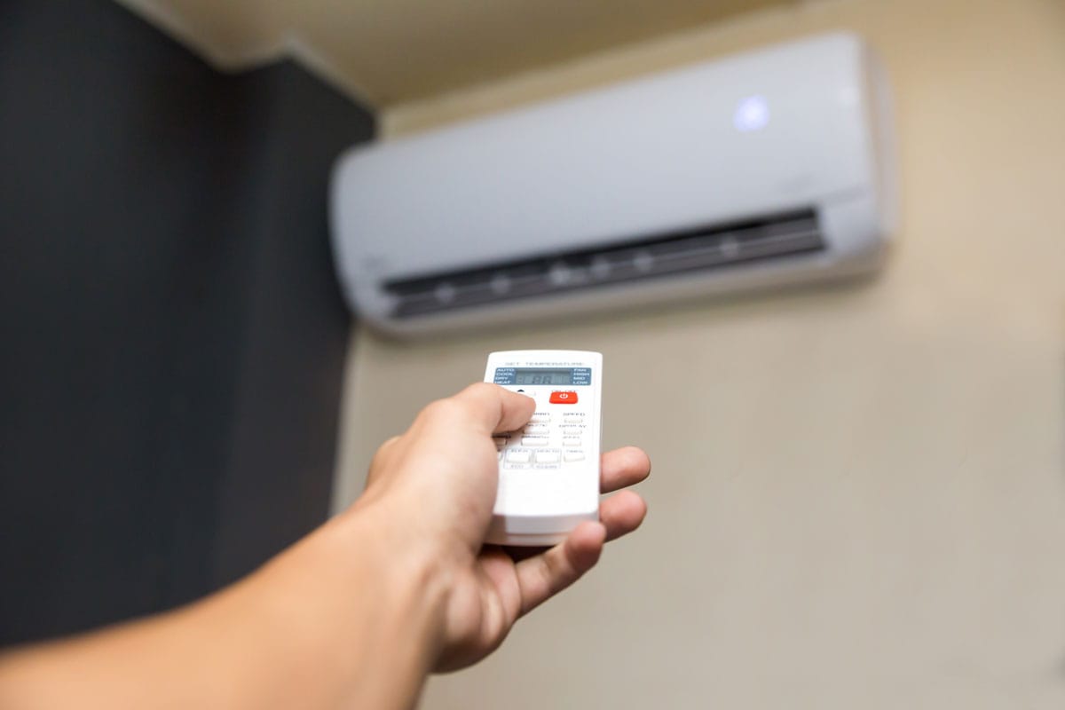 man's hand holding air conditioning unit remote control aimed at the AC unit