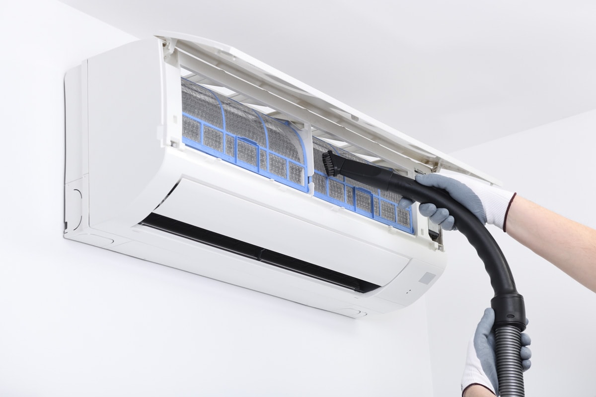 A worker is using a vacuum cleaner to clean the air conditioner.Air conditioner system on white wall room. Air conditioning.A white air conditioner is installed on a white wall in the apartment.