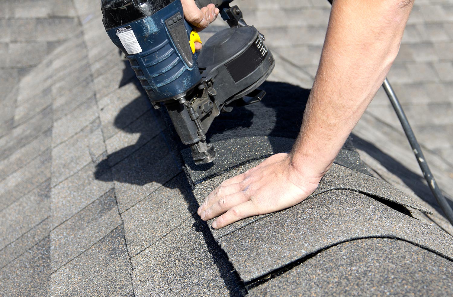 A roofer nails shingles over ridge vent material used on the peak of new residential house construction
