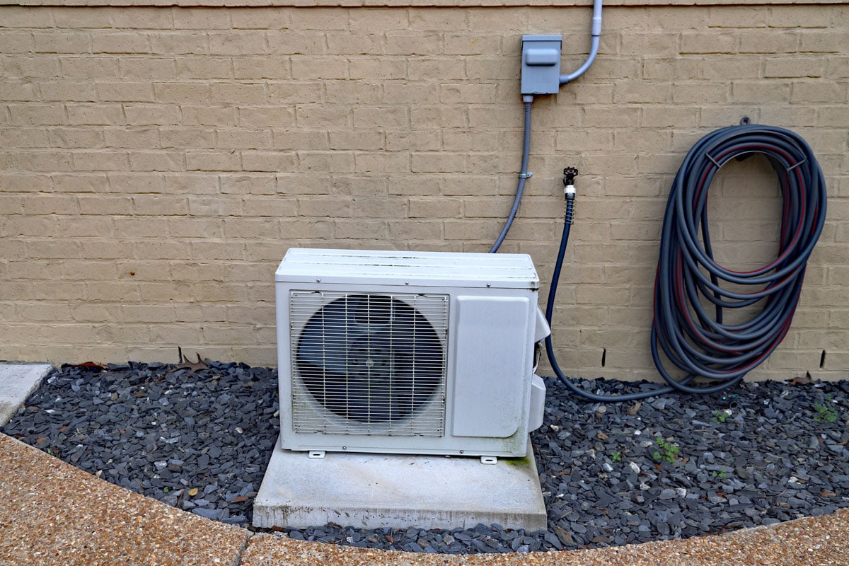 A white air conditioner inverter mounted on a concrete slab