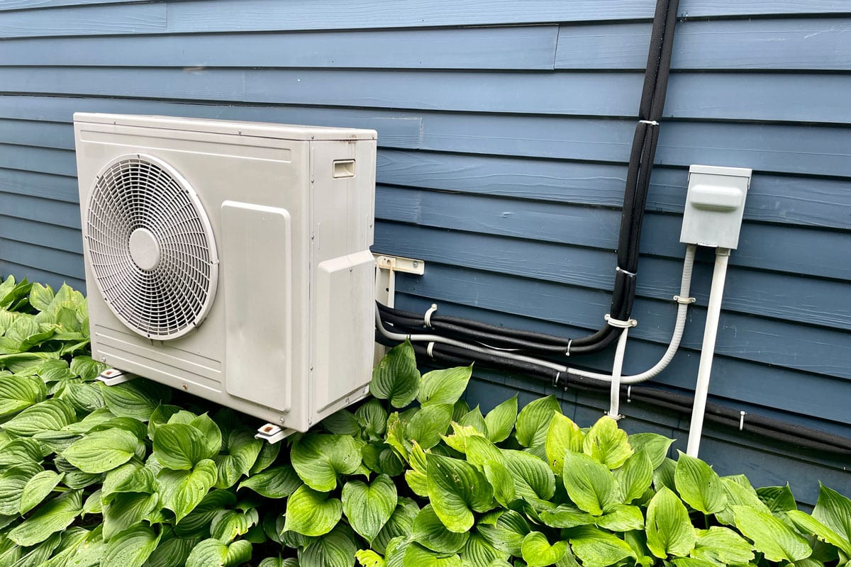An air conditioner mounted on a metal bracket on the side of a house