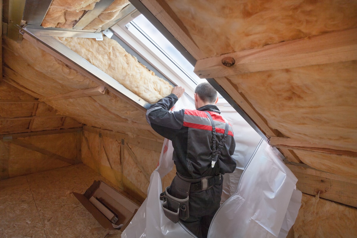 Back view of roofer builder worker installing vapor barrier around the skylight opening in attic of new house under construction