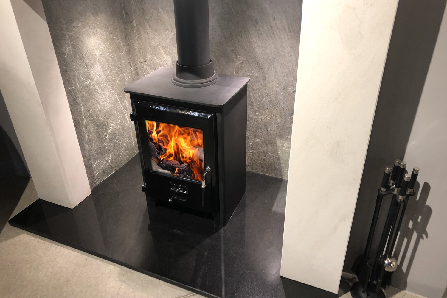 Image of square cast iron woodburner contemporary log wood burning stove fireplace mantle with orange fire flames burning and generating heat to warm up room instead of gas boiler central heating, modern multifuel stove wood burner stand chimney flue