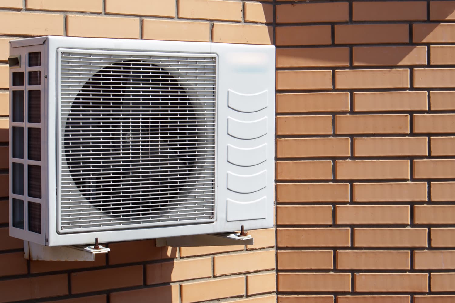 Close-up shot of a modern climate control unit against the background of a brick wall of the facade of a house outside. Air conditioner on the wall with space for text. Air compressor