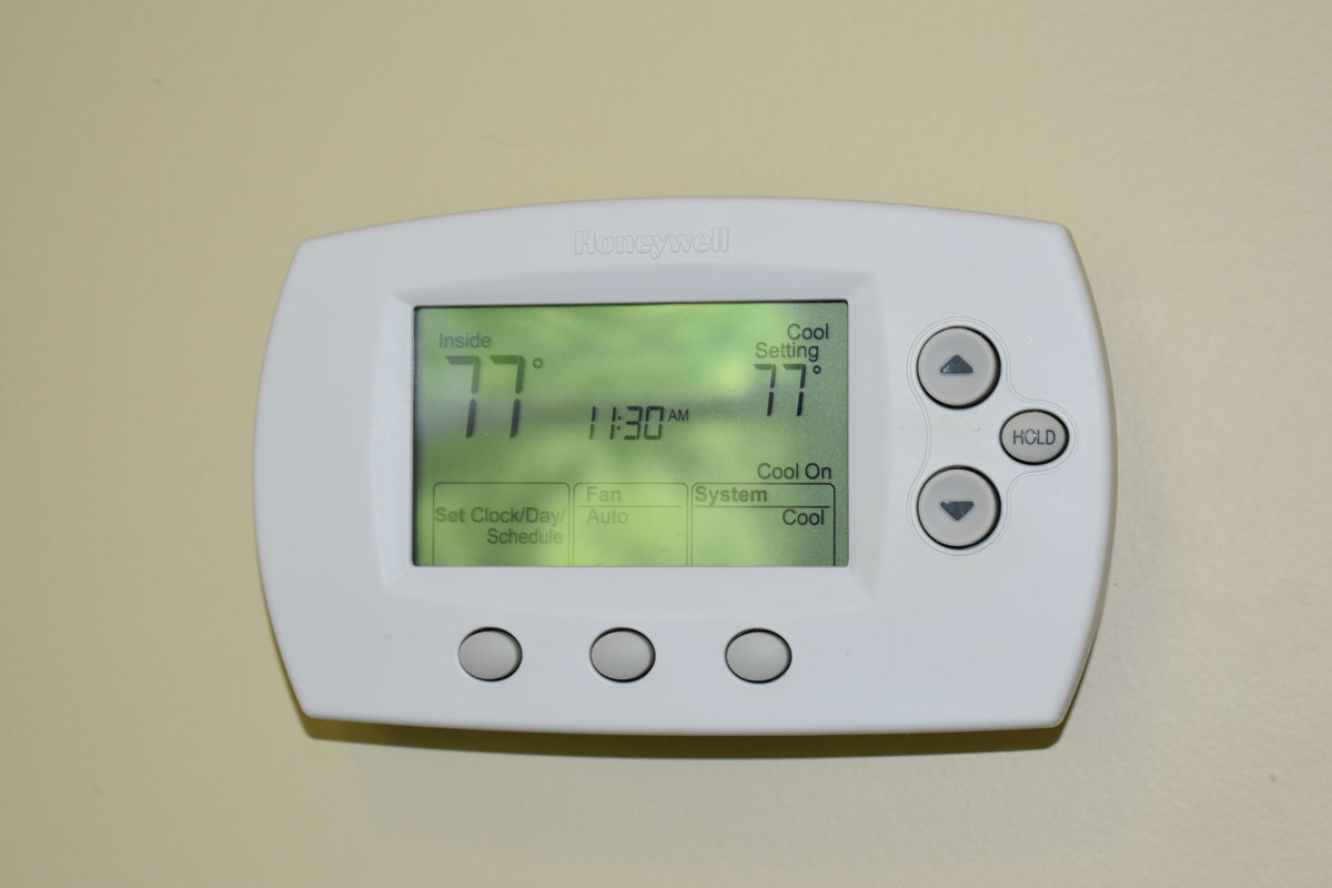 Honeywell digital thermostat set to 77 degrees Fahrenheit, with trees reflected