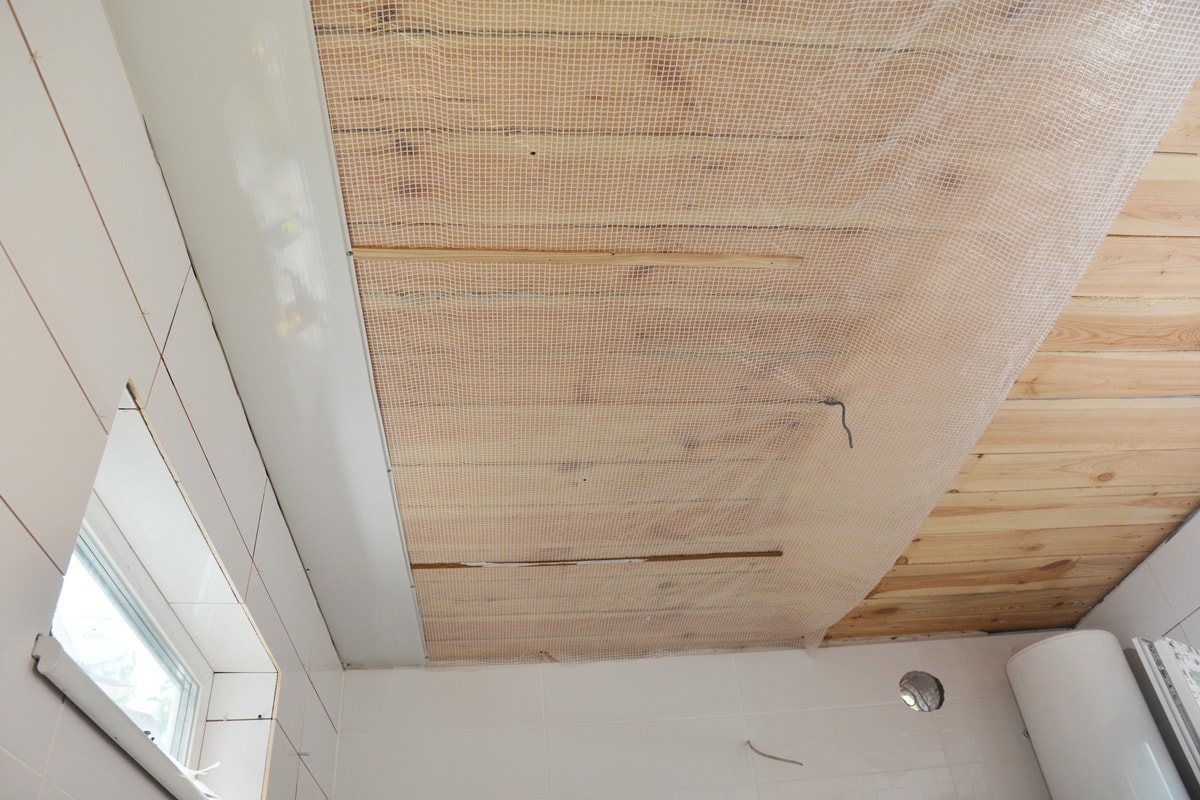  Installing PVC ceiling cladding, plastic ceiling panels over a vapor barrier membrane and planked wood ceiling in a bathroom.
