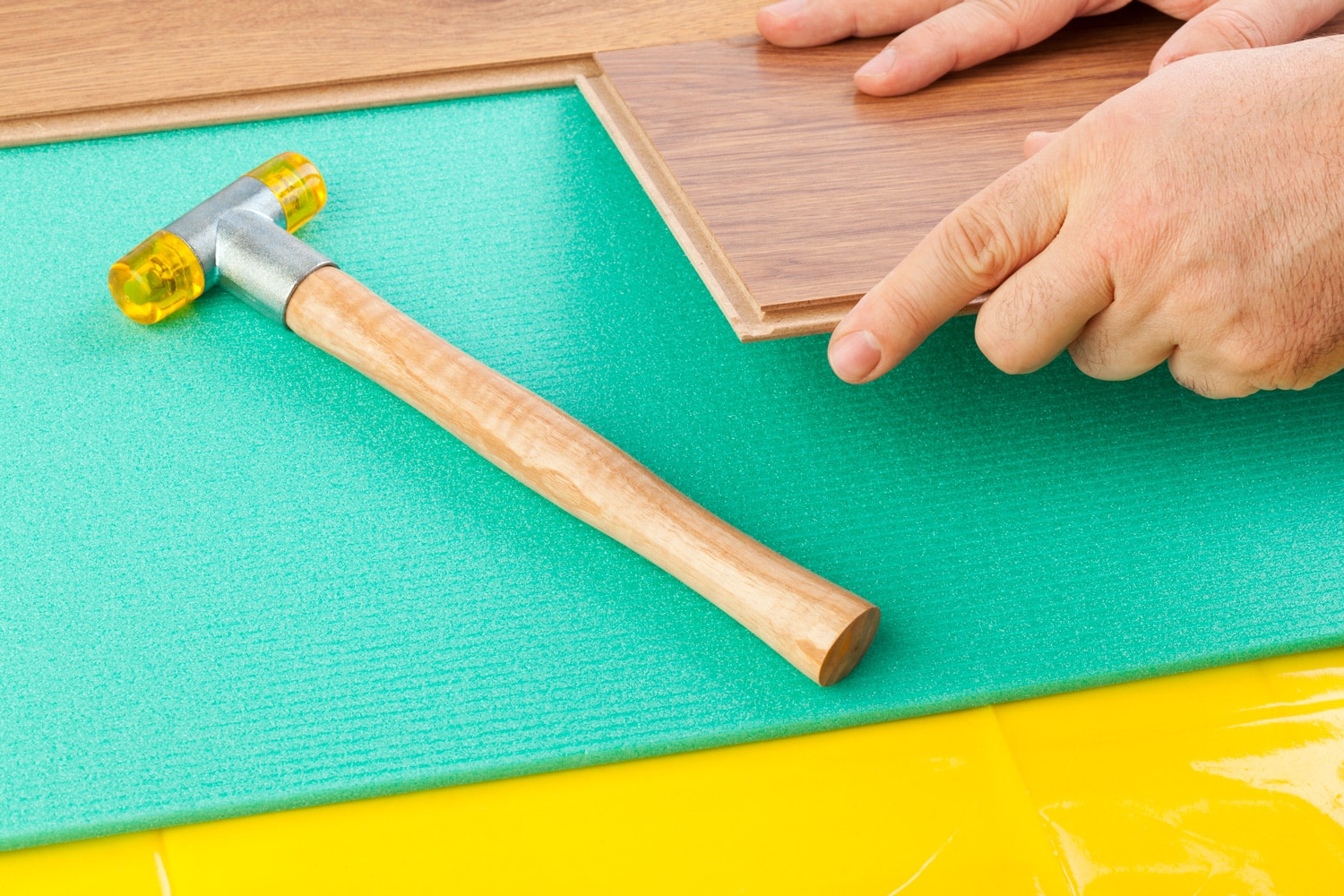 Laying Laminate Flooring. Yellow film vapor barrier and green foam underlayments. Person's hand seen putting the planks together.
