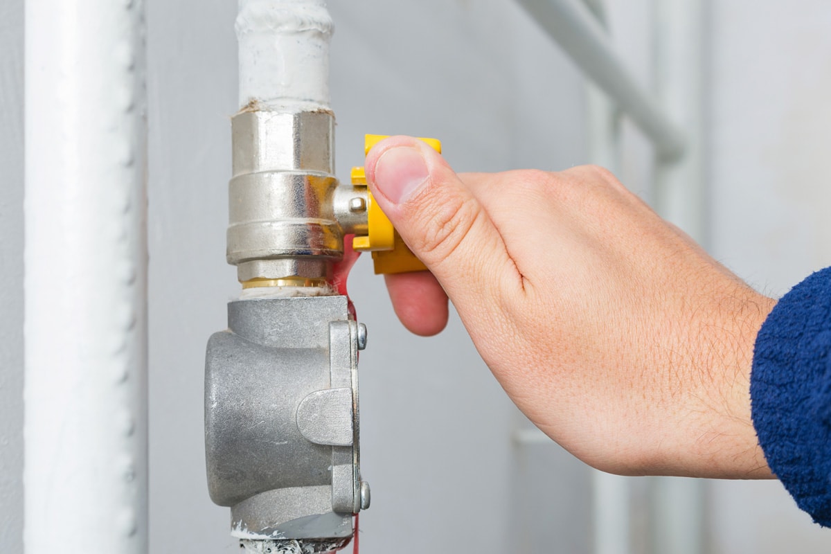 Male hand opens or closes natural gas valve in home boiler room