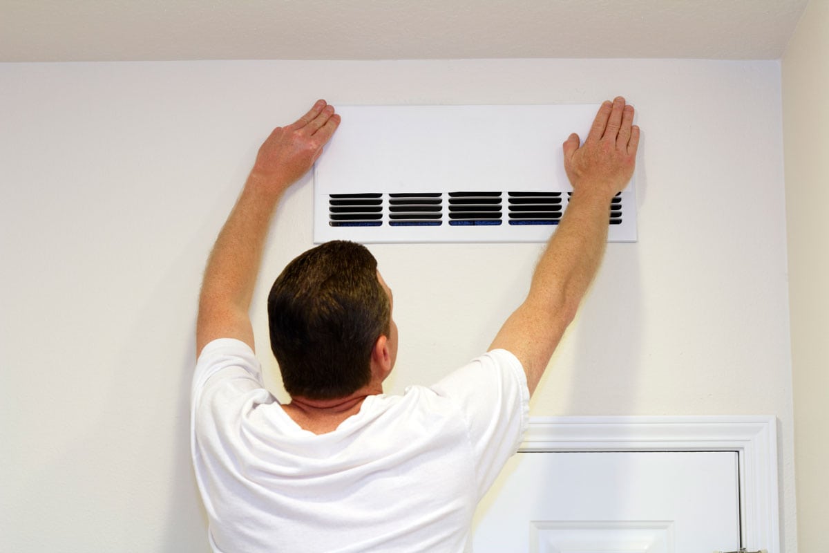 Male placing a paper cover over part of an air return intake vent to increase air return in another vent