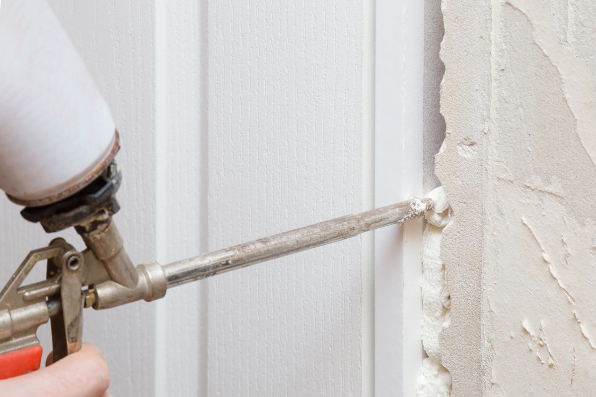 Man hands using spray gun and filling gap with construction foam between new door and wall.