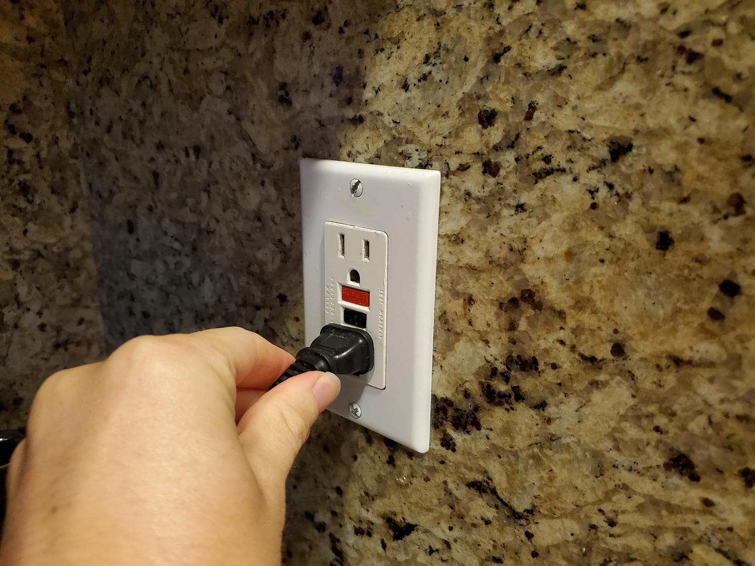 Man plugging an electrical cord into a Ground Fault Circuit Interrupter (GFCI) electrical outlet on the wall