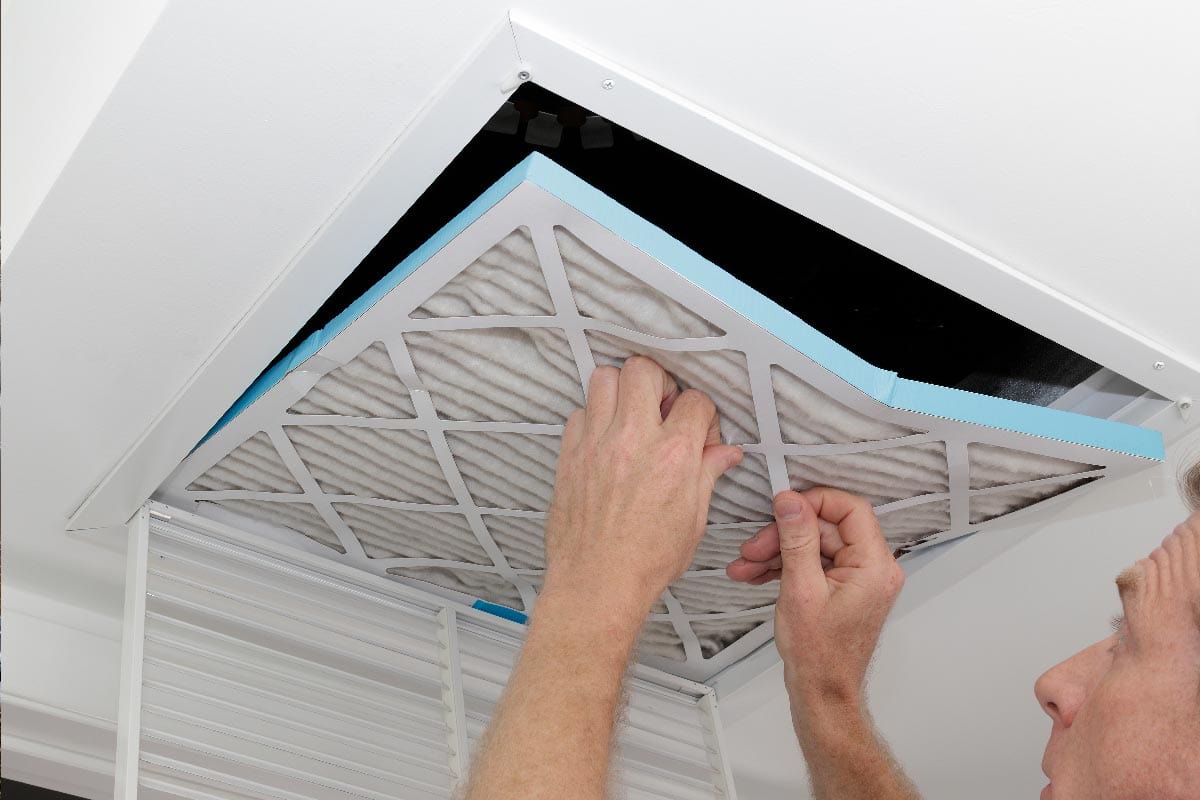 A person removing an old dirty air filter from a ceiling intake vent