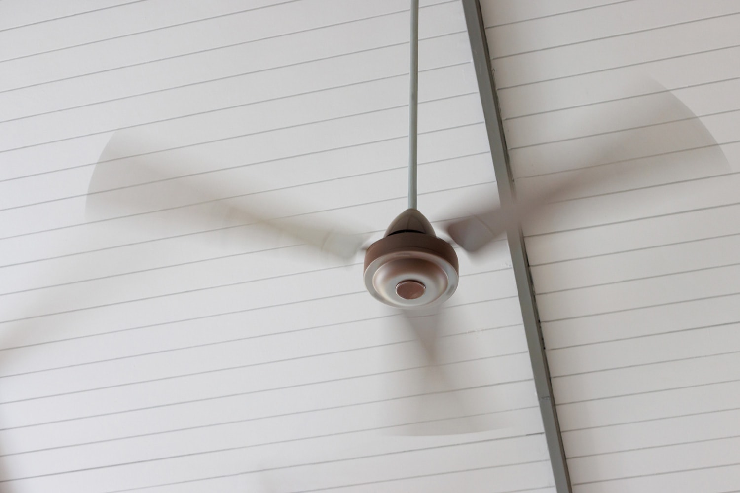 Moving brown ceiling fan on white ceiling in house.