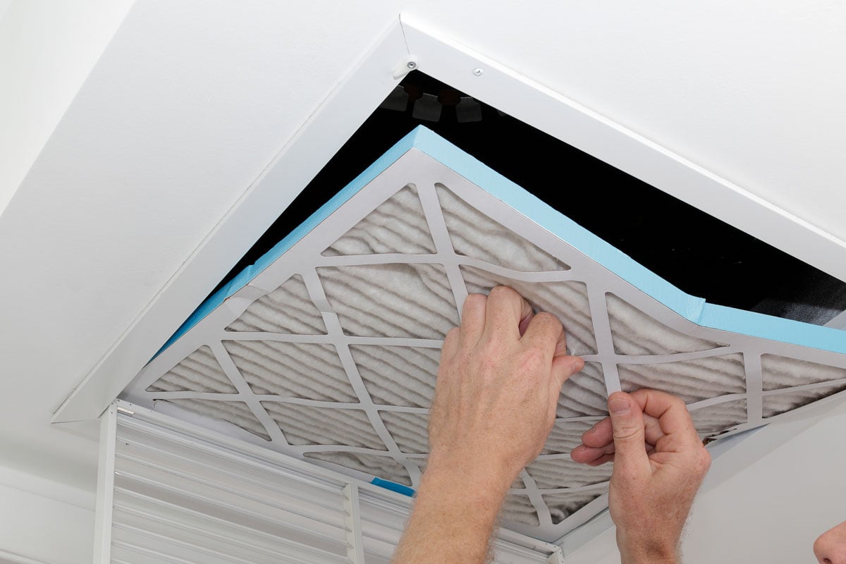 Person removing an old dirty air filter from a ceiling intake vent of a home HVAC system