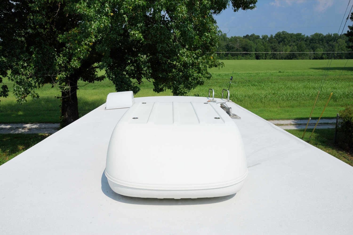 Photograph on roof of recreational vehicle looking into large field. RV roof has large air conditioning unit, ladder, and roof vents.