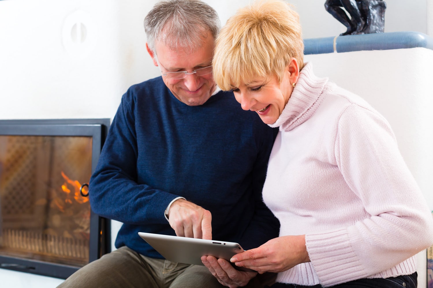 Quality of life - two elderly people sitting at home in front of the furnace, writing emails on the tablet computer