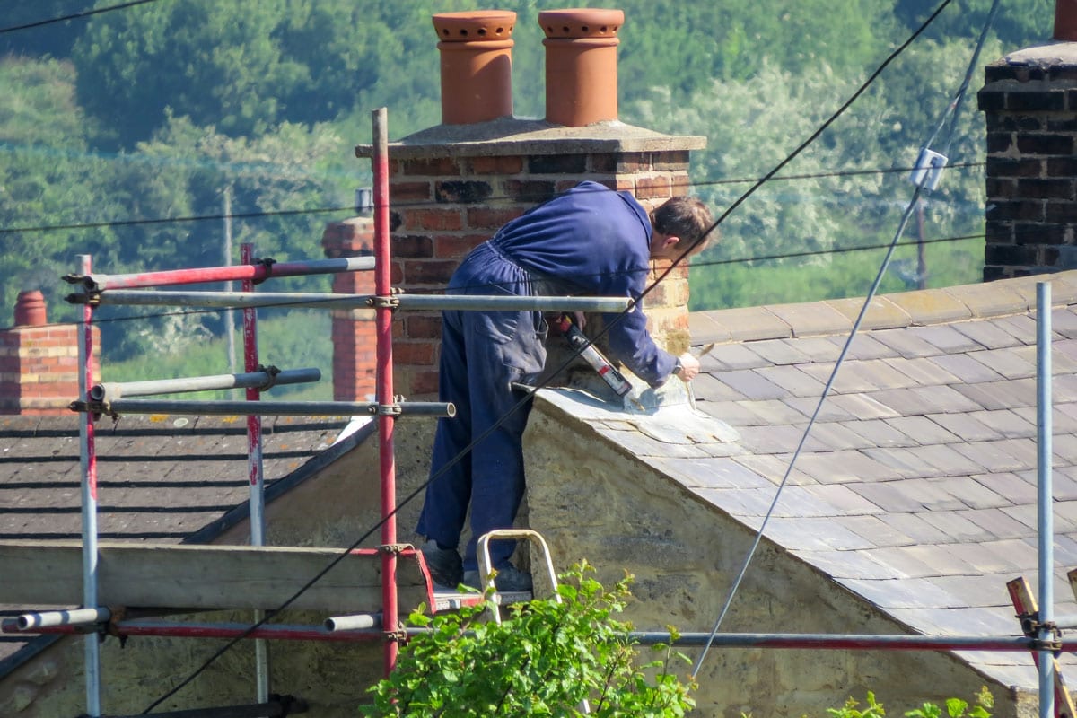 Roofer repairing flashing on chimney stack on a slate roof of a domestic house