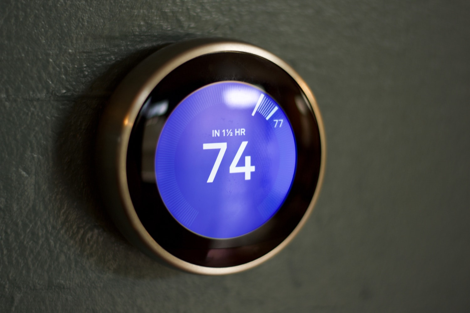 Smart thermostat being adjusted by male hand against a blue wall. Smart thermostat on dark blue wall. Small reflection present